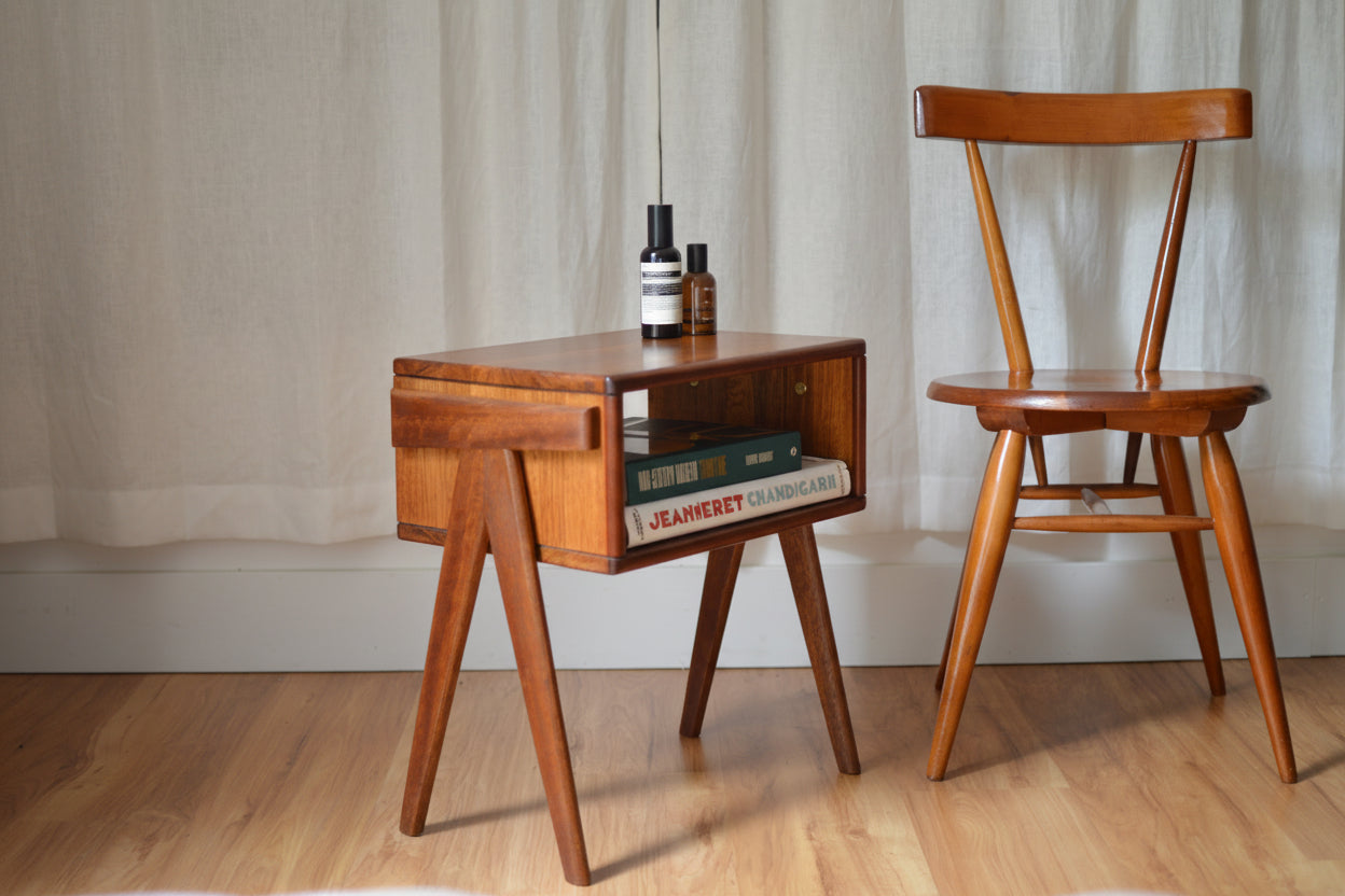 A mid-century modern style bedside table with a brown Tasmanian oak top and brown merbau wood legs.